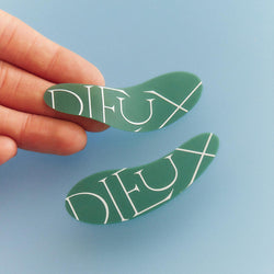 Model's hand holding Dieux Forever Eye Mask on a blue background.