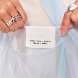 Close up of hands holding The Dieux-It-All Tote . The tag reads "Clearly there's nothing you cant handle."