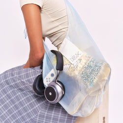 A model carrying The Dieux-It-All Tote, filled with typical things you might find in a bag: snacks, headphones, shoes. 
